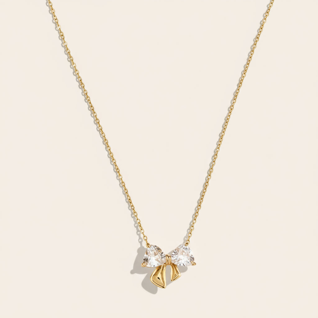 A delicate gold necklace with a pendant featuring a bow and two small stones.